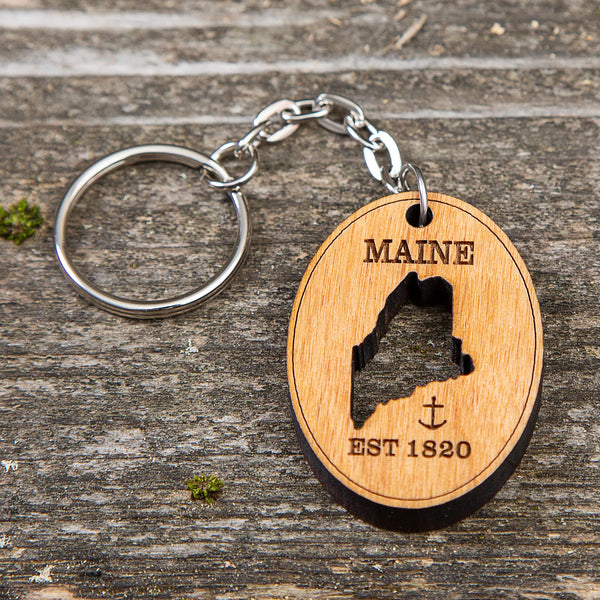 163 Design Company metal keyring with attached wooden oval piece with state of Maine cutout of middle with word MAINE and EST 1820 and anchor