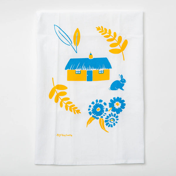 The white tea towel features yellow ferns, a yellow house with a blue roof, a blue bunny, and blue flowers
