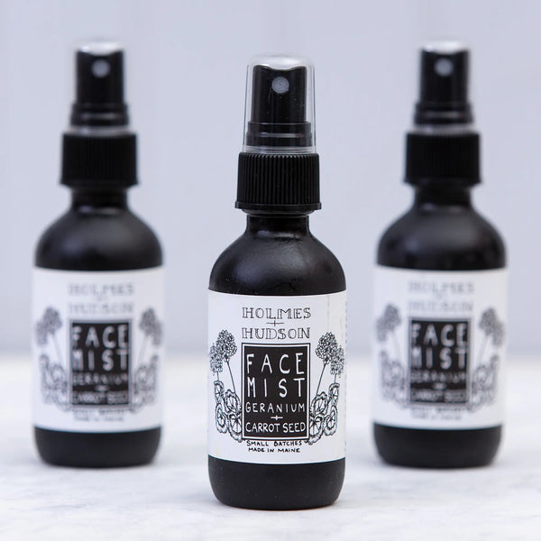 Opaque black bottles of geranium & carrot seed face mists with spray tops