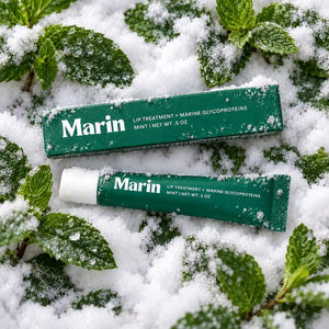 Marin Skincare Mint Lip Treatment tube with fresh mint leaves beside it, showcasing a hydrating lip balm product.