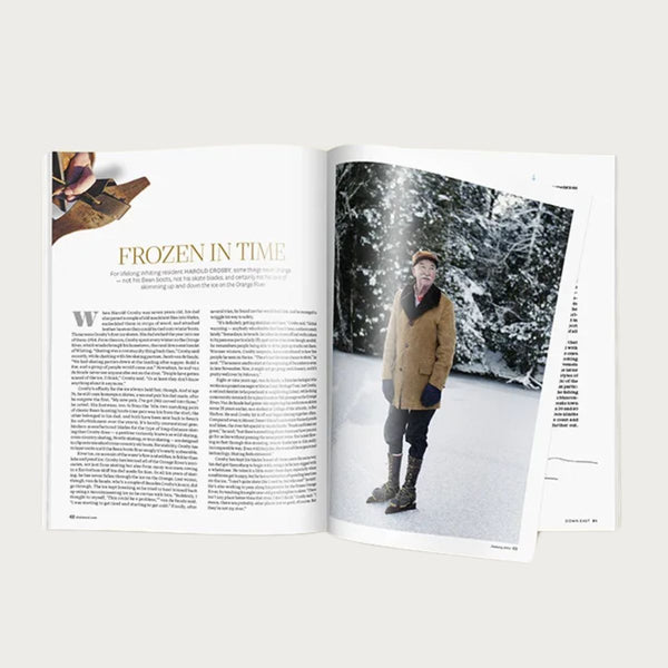 A person reading a Down East Magazine subscription issue outdoors, showcasing the magazine's cover and engaging in leisure reading.