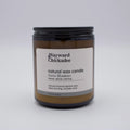 Wayward Chickadee Swiss Meadows scented candle in a glass jar with a lit wick and floral design, emitting a warm, inviting glow