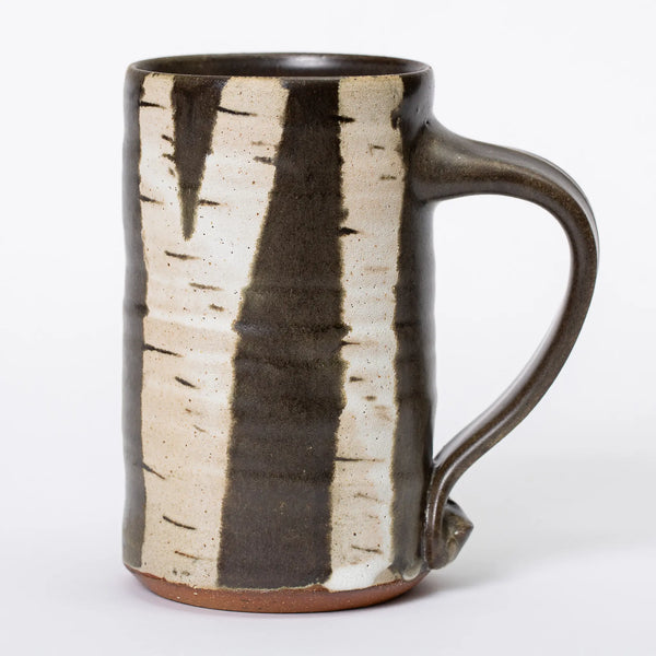 From the side, there are multiple branching birch trees in white glaze on the black handled mug