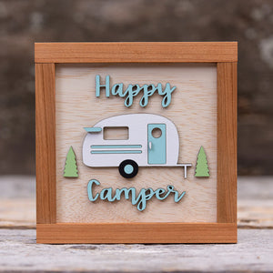 163 Design Company wooden frame and background with painted wooden camper, 2 pine trees, and the word Happy Camper