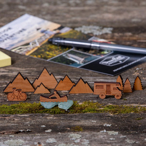 163 Design Company small wooden pieces include camper, canoe, bicycle, mountains, and pine trees