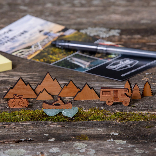 163 Design Company small wooden pieces include camper, canoe, bicycle, mountains, and pine trees