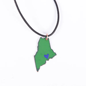 Blueberry Bay Jewelry green state of Maine copper enameled necklace hangs from a black leather cord with a small blue heart design on the coast
