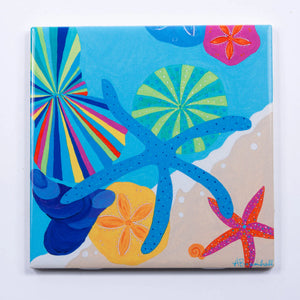 Festive Fish brand festive trivets featuring colorful shell designs on a wooden surface.