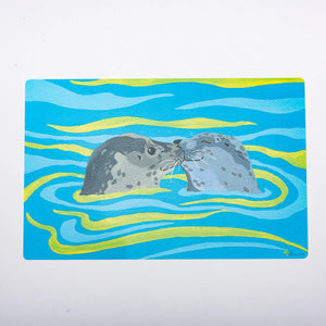 Two festive fish-themed placemats featuring playful seal illustrations, perfect for holiday dining decor.