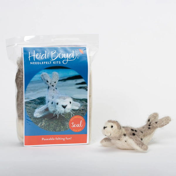 Poseable harbor seal needlefelt kit in clear plastic package next to completed example