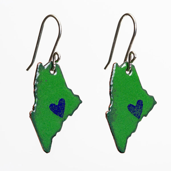Blueberry Bay Jewelry tilted view of green state of Maine copper enameled earrings hang from sterling silver ear wires and each one has a small blue heart design on the coast
