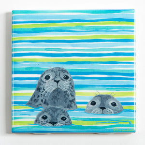 Three colorful Festive Fish tile coasters featuring playful seal illustrations, perfect for holiday decor and table protection.