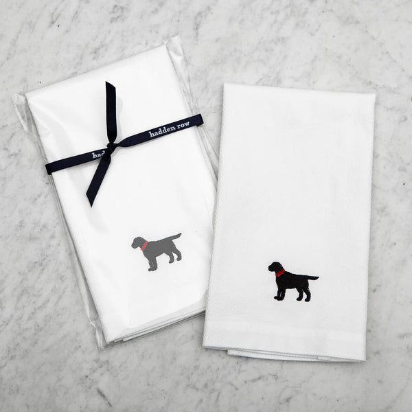 two white tea towels with an embroidered black lab with a red collar on a marble background