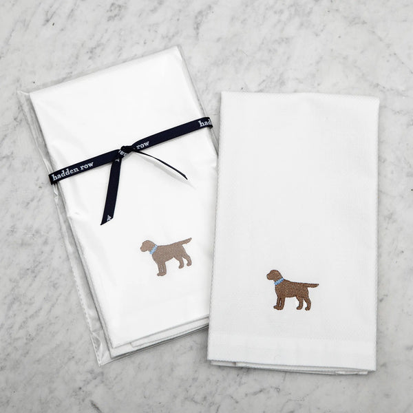 two white tea towels with an embroidered chocolate lab with a blue collar on a marble background