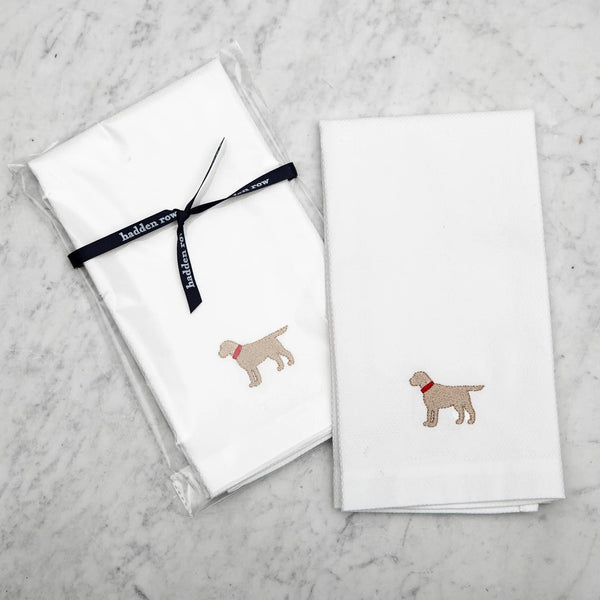 two white tea towels with an embroidered yellow lab with a red collar on a marble background