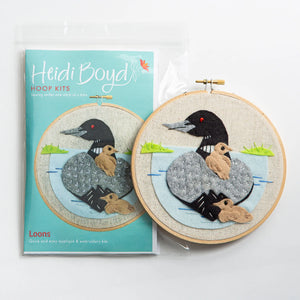 Loon hoop kit in clear plastic package next to completed example with mother loon and two babies