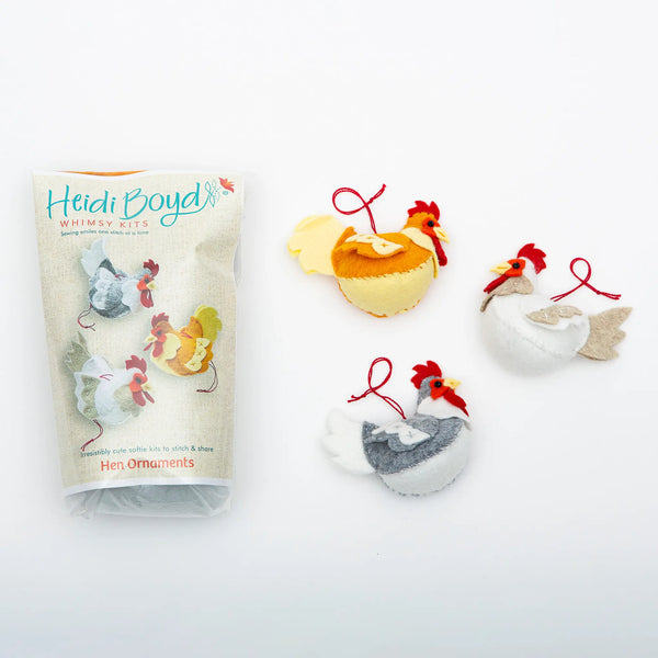 Hen ornament felting kit in clear plastic package next to completed examples of three hens