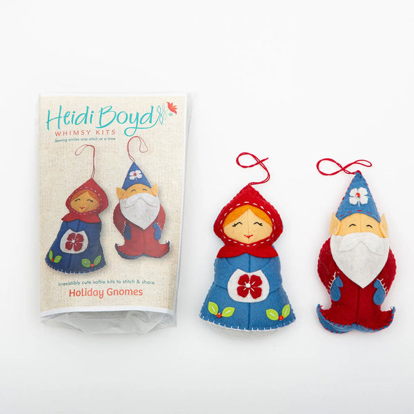 Holiday gnomes ornament felting kit in clear plastic package next to completed examples of two gnomes