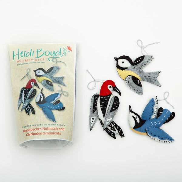 Maine bird ornament felting kit in clear plastic package next to completed examples of three woodland birds