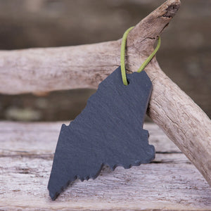 A slate Maine ornament by A&E Stoneworks displayed on driftwood, showcasing natural gray slate with engraved design.
